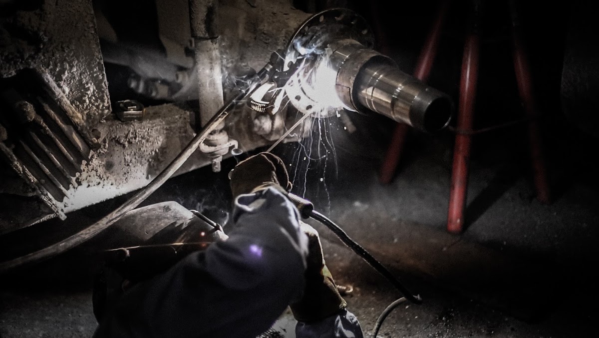 Close-up of a welder repairing a vehicle frame underneath a car